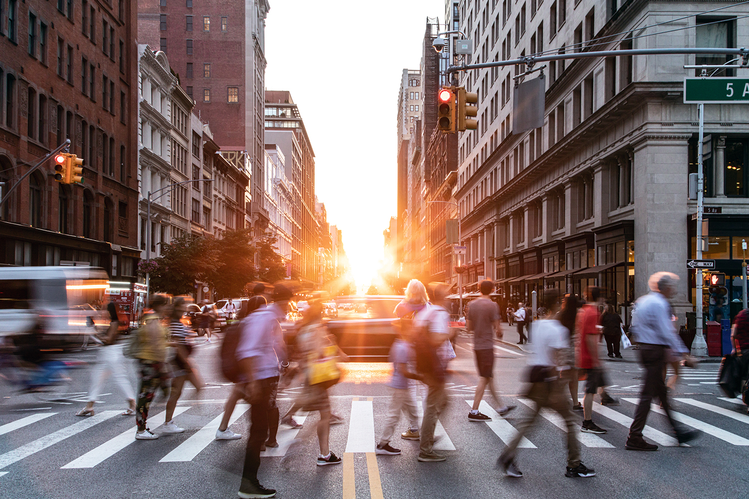 Diverse crowds of people walking through a busy intersection on 5th Avenue and 23rd Street in New York City with sunset in background