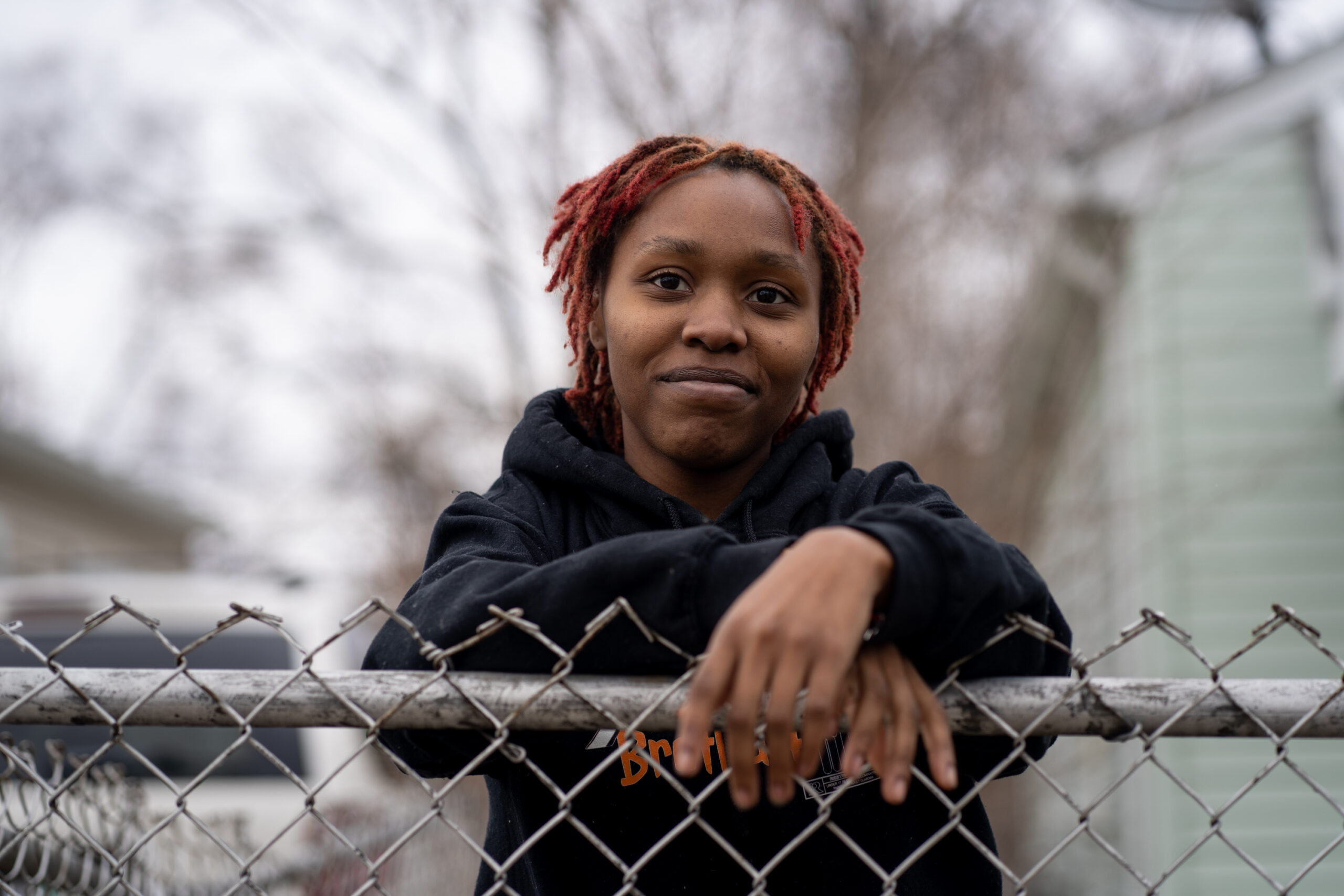 A girl posing at a fence with a slight smile.