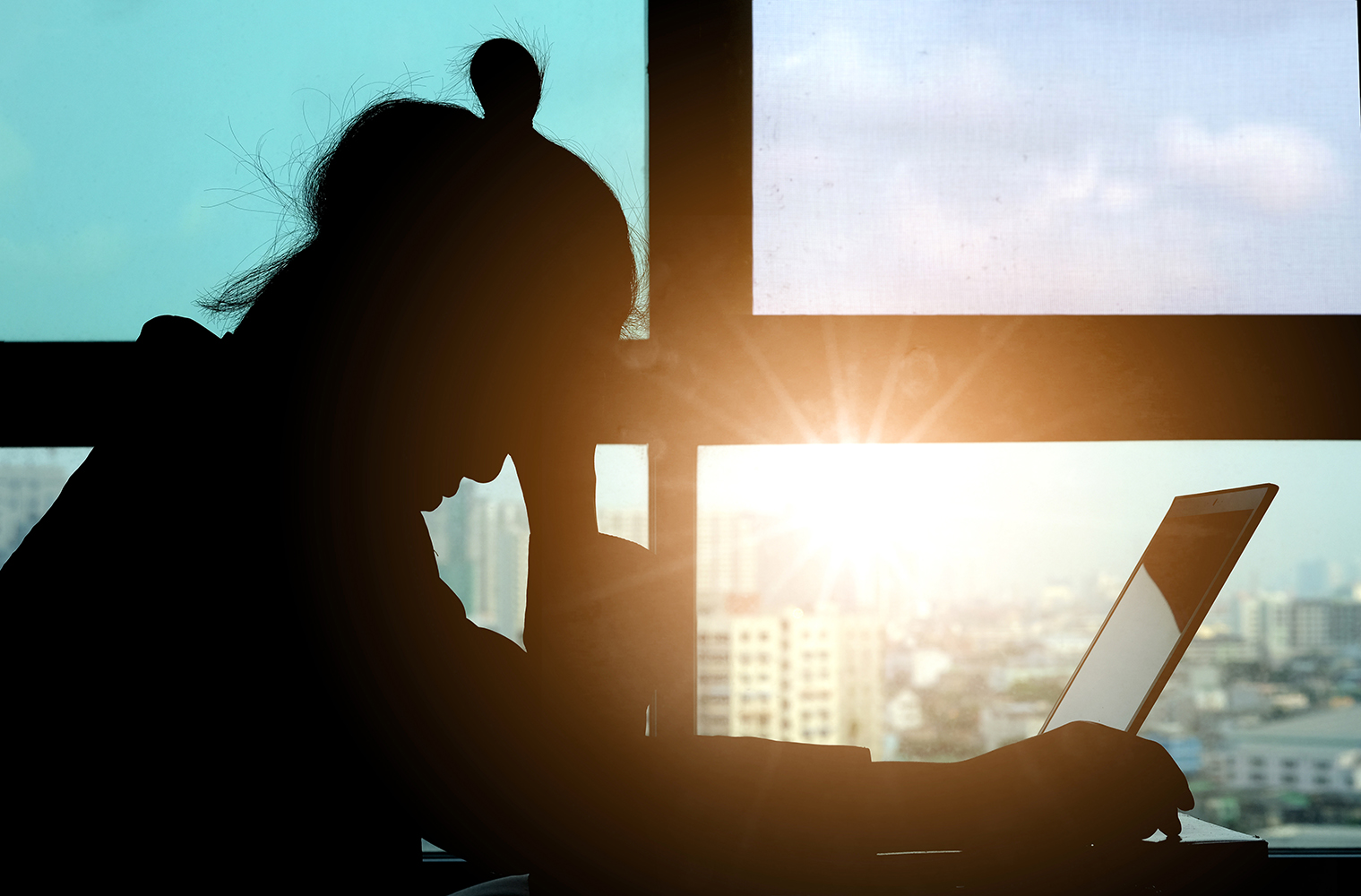 A woman sitting at her laptop, stressed, with sun rising through the window